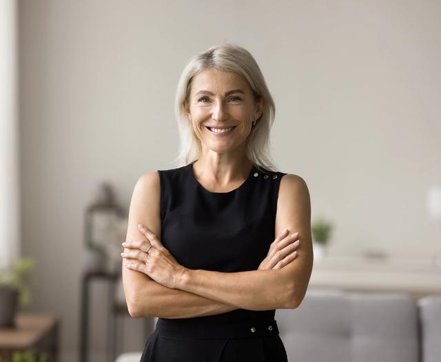 a woman in a black dress is standing with her arms crossed and smiling .