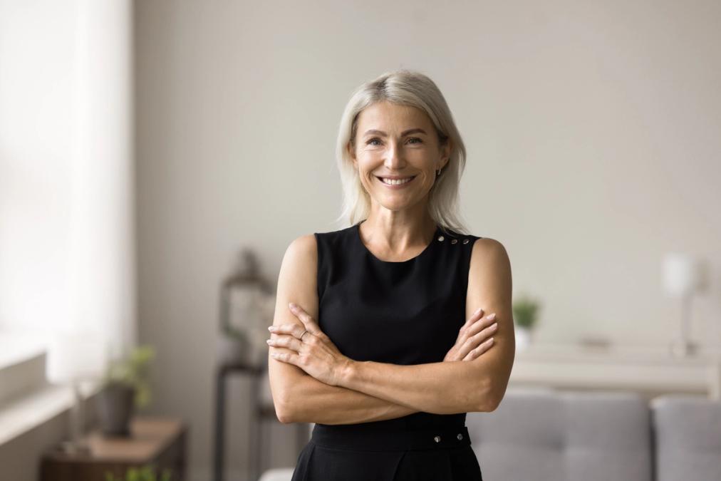 a woman in a black dress is standing with her arms crossed and smiling .