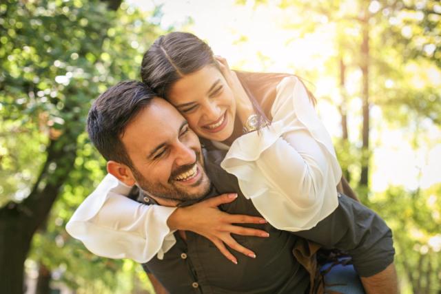 a man is carrying a woman on his back in a park .