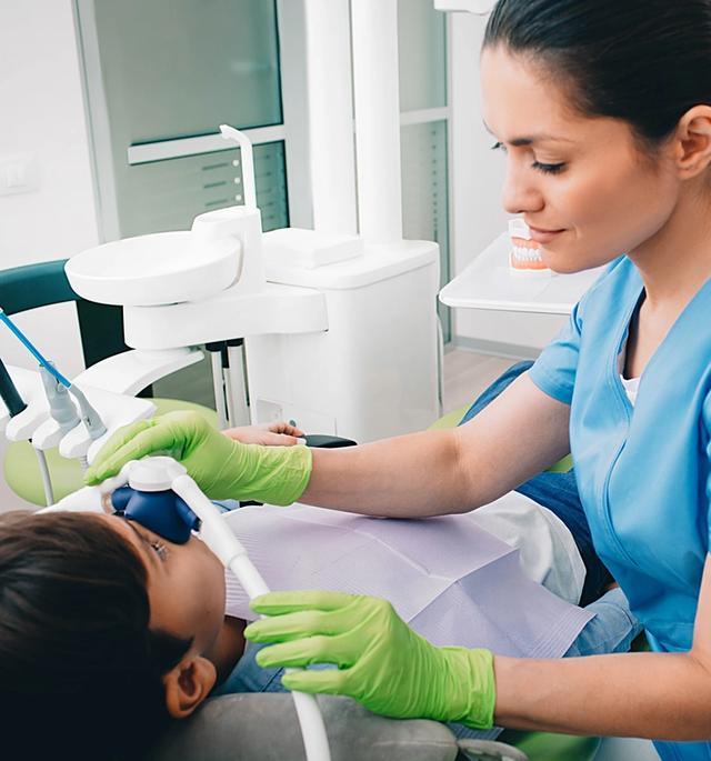 a female dentist is examining a young boy 's teeth in a dental office .