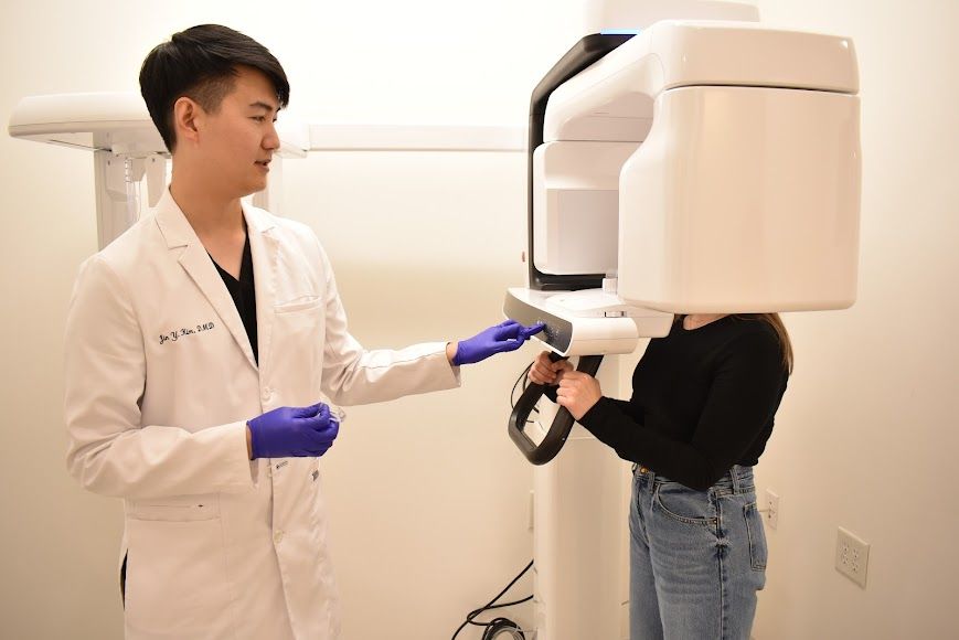 A dentist helps a patient use a white dental imaging machine.