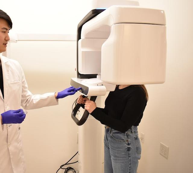 A dentist helps a patient use a white dental imaging machine.