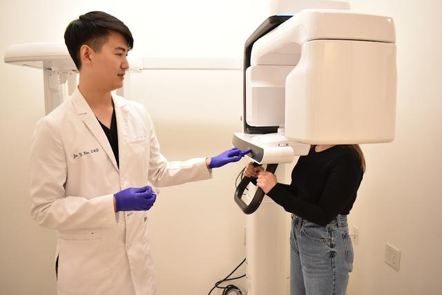A dentist assists a patient positioned in a panoramic dental X-ray machine.
