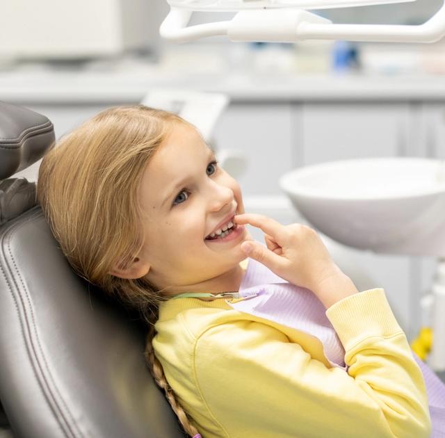 a little girl is sitting in a dental chair and smiling at the dentist .
