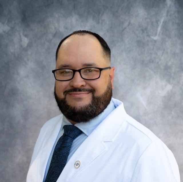 a man with a beard and glasses is wearing a white coat and tie .