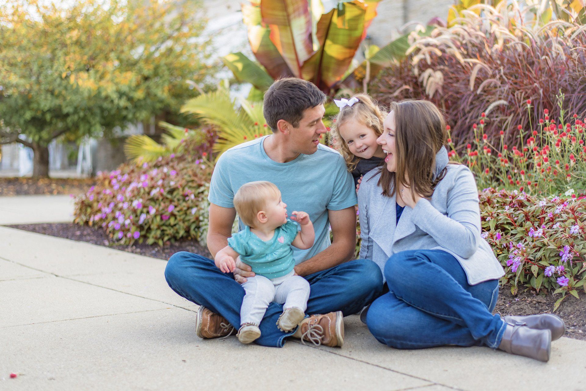 a family is sitting on the sidewalk with a baby .