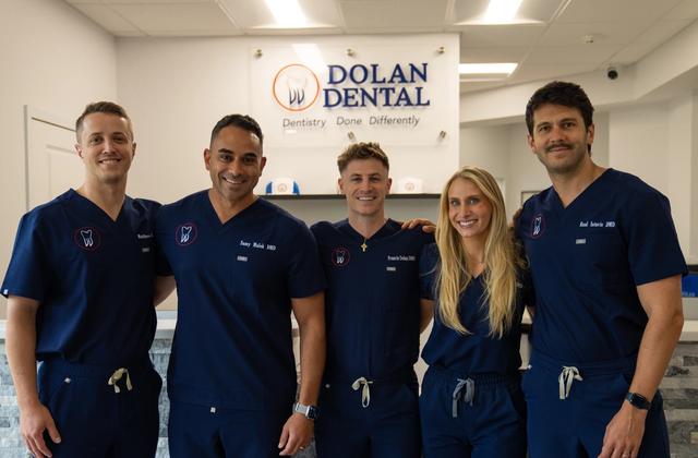 a man in a scrub is smiling in front of a dental sign .