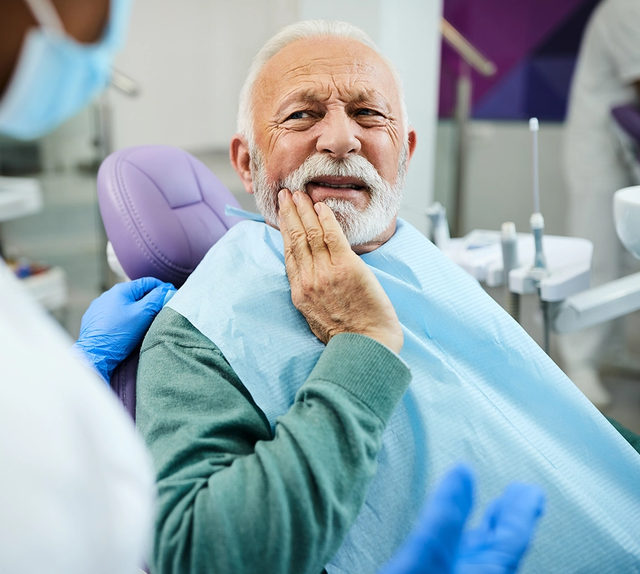 an older man is sitting in a dental chair with his hand on his mouth