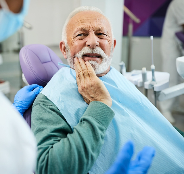 an older man is sitting in a dental chair with his hand on his mouth