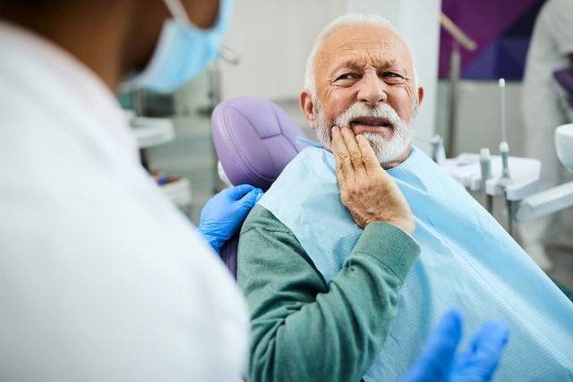 an older man is sitting in a dental chair with his hand on his mouth