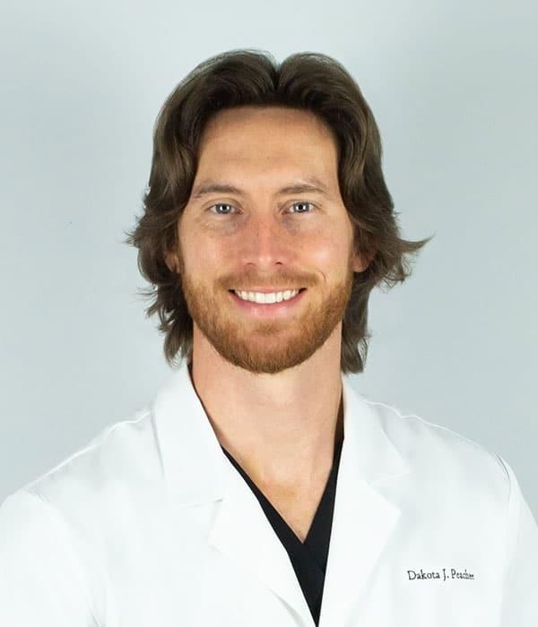 Portrait of Dakota J. Preacher, a smiling man with brown hair and a beard, wearing a white lab coat.