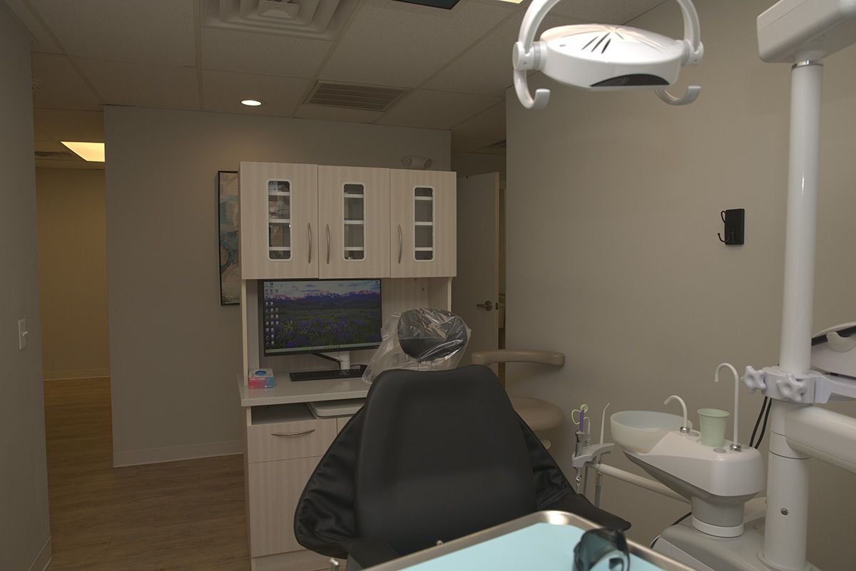 A modern, empty dental examination room with a black chair, dental equipment, and a computer workstation.