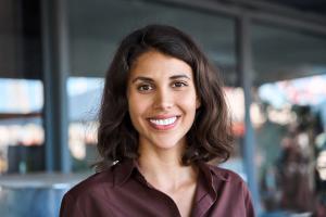 Smiling woman with dark wavy hair and a brown collared shirt.