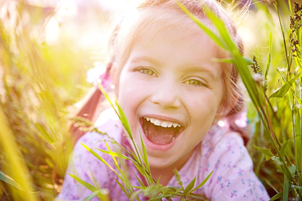 a little girl is laying in the grass and laughing.