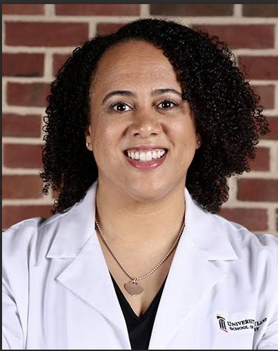 a woman in a white lab coat is smiling in front of a brick wall .
