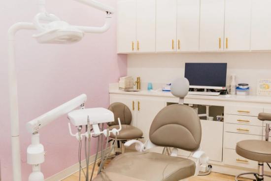 A modern dental exam room with pink walls, a tan dental chair, and white cabinets.