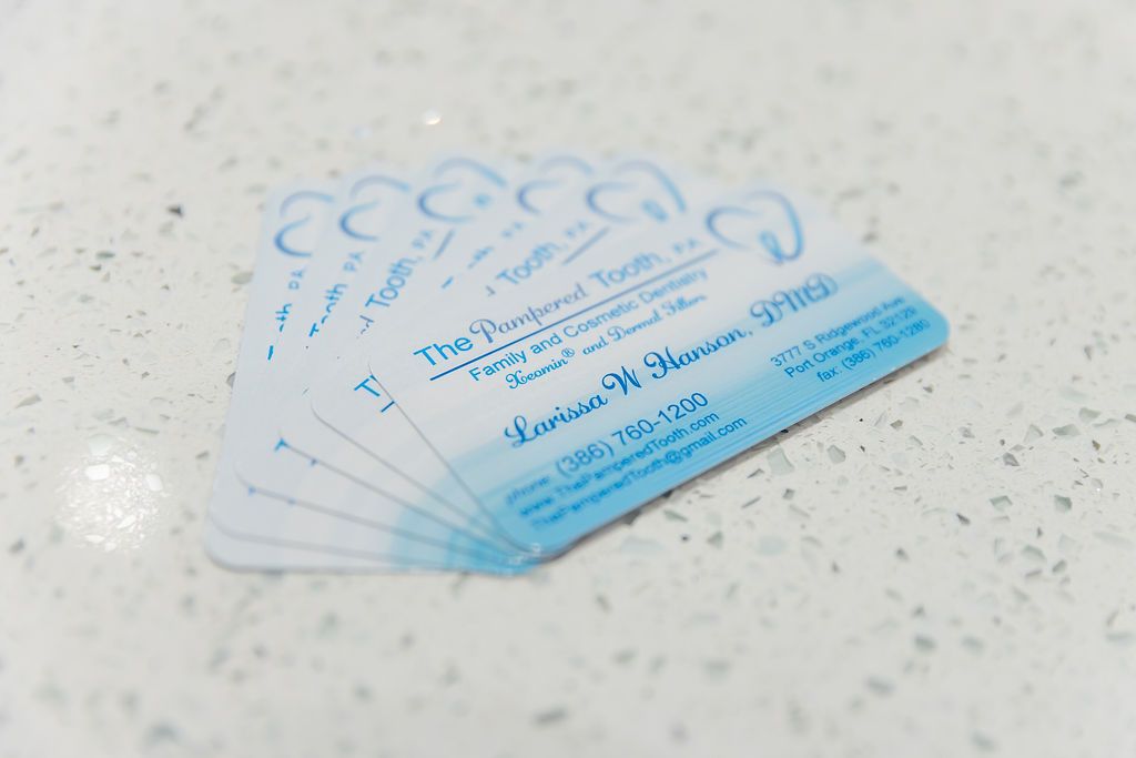 A fanned stack of business cards for "The Pampered Tooth" dentistry, featuring a blue tooth logo and contact information.