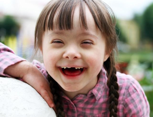 a little girl with down syndrome is smiling with her eyes closed .