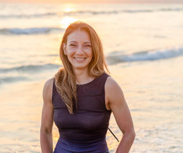 Smiling woman standing in front of the ocean at sunset.
