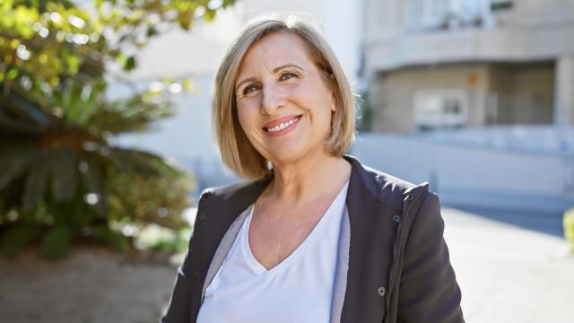 a woman is smiling while standing on a sidewalk in front of a building .