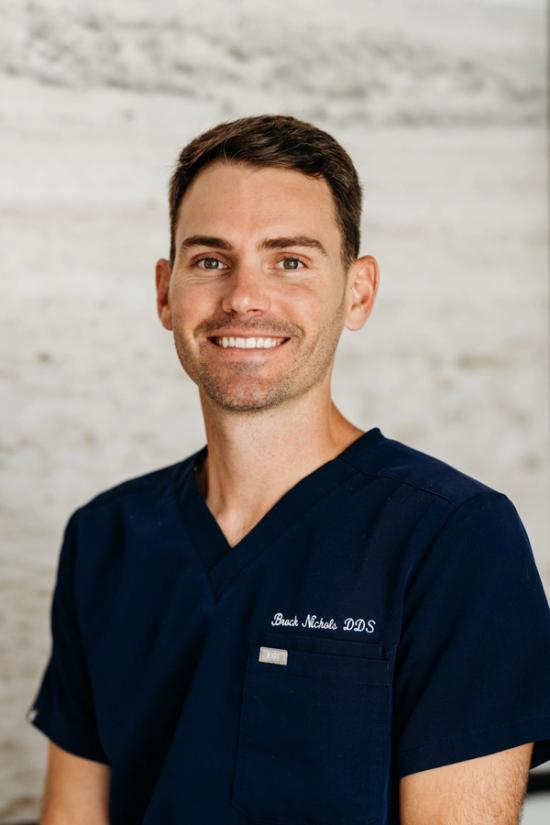 A smiling man in navy blue scrubs with "Brack Nichols DDS" embroidered on the chest.