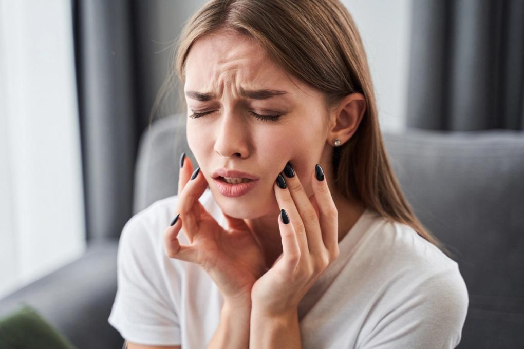 a woman is sitting on a couch holding her face in pain because of a toothache .