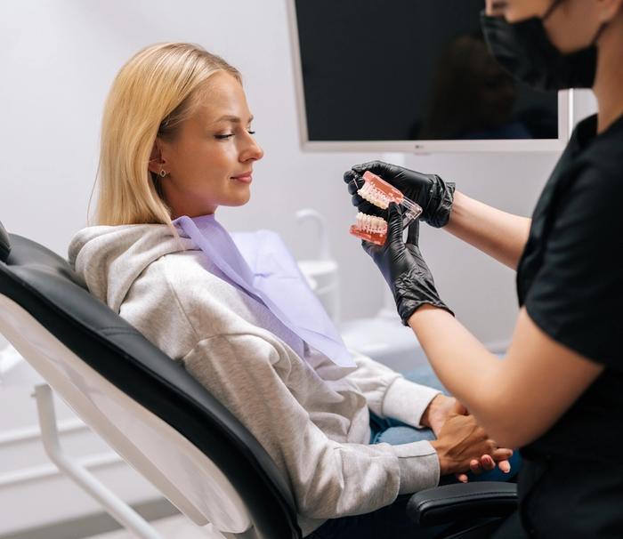 a woman is sitting in a dental chair while a dentist shows her a model of her teeth .
