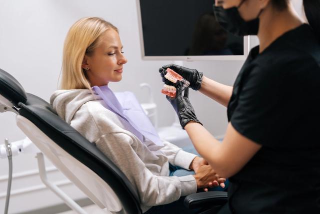 a woman is sitting in a dental chair while a dentist shows her a model of her teeth .