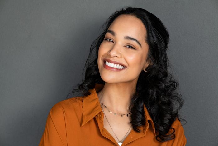 a woman in an orange shirt and necklace is smiling .