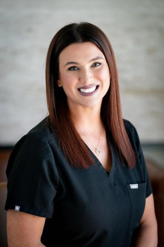 a woman wearing a black scrub top and a necklace smiles for the camera .