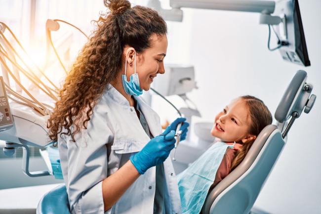 a female dentist is examining a little girl 's teeth in a dental chair .