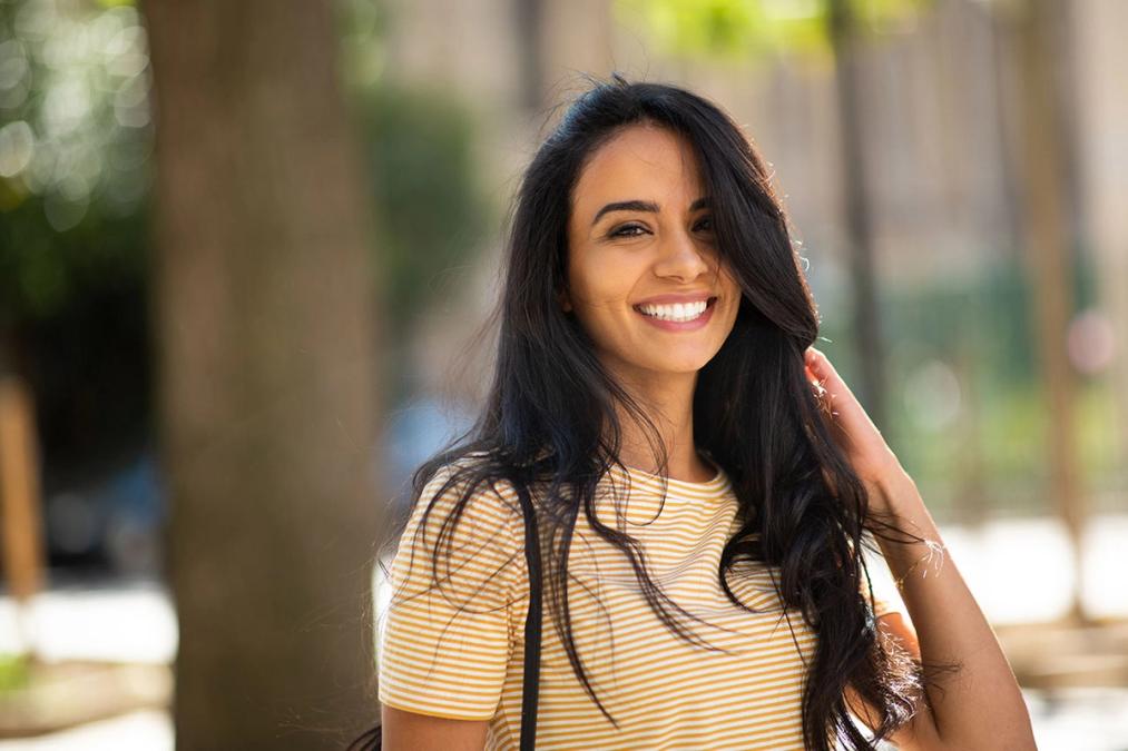 a woman in a yellow and white striped shirt is smiling and touching her hair .