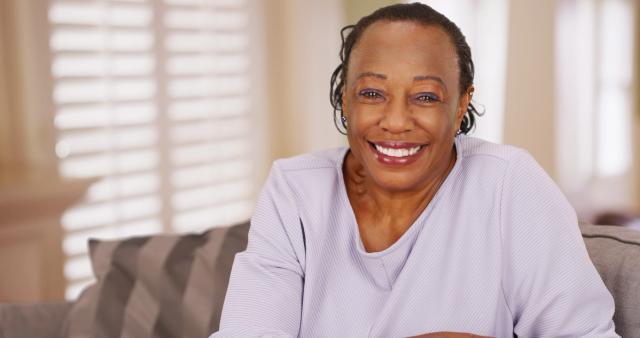 an elderly woman is sitting on a couch smiling at the camera .