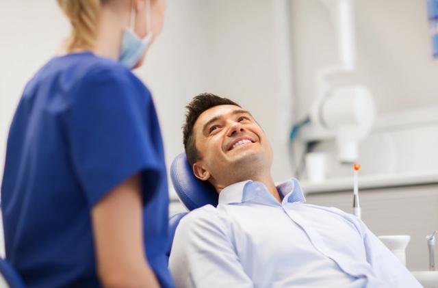 a man is sitting in a dental chair talking to a female dentist .