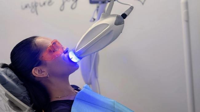 A woman receiving teeth whitening treatment with a blue light and protective eyewear.
