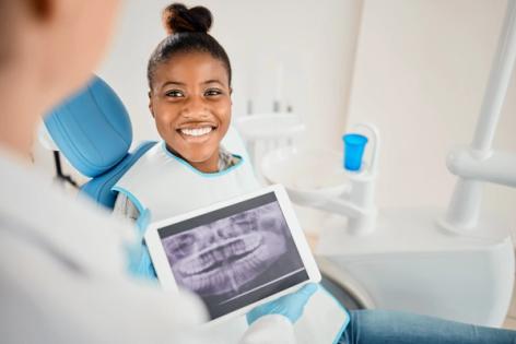 a woman is sitting in a dental chair holding a tablet with an x-ray of her teeth on it .