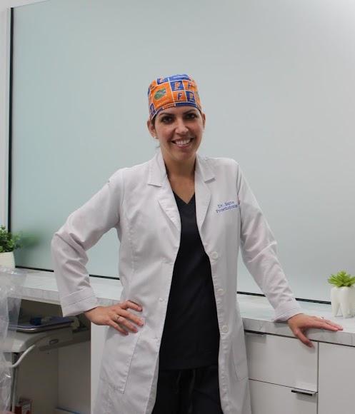 a woman in a lab coat and hat is standing in a dental office .