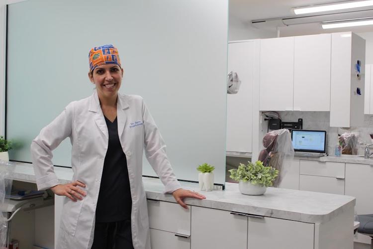 a woman in a lab coat and hat is standing in a dental office .