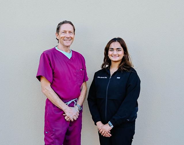 a man and a woman standing next to each other with the man wearing a pink scrub top