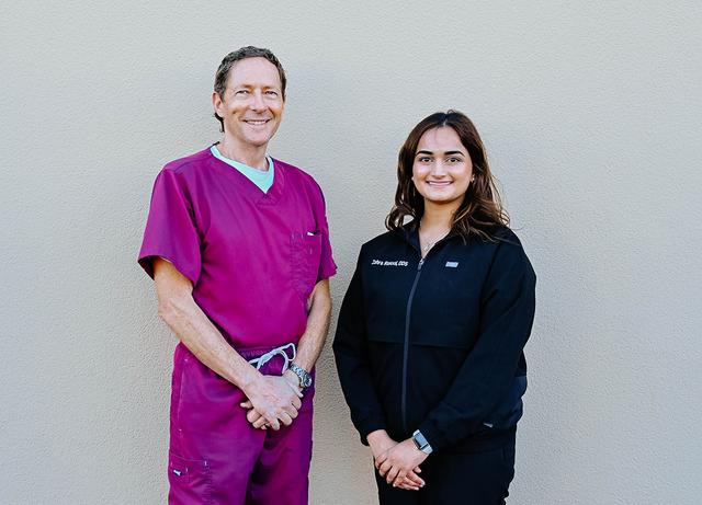 a man and a woman standing next to each other with the man wearing a pink scrub top