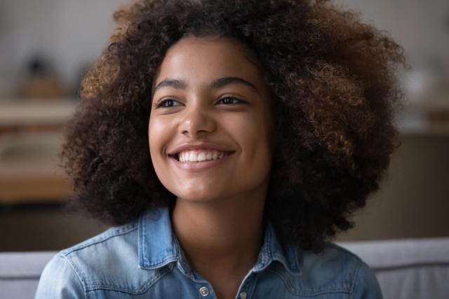 a young woman with curly hair is smiling while sitting on a couch .