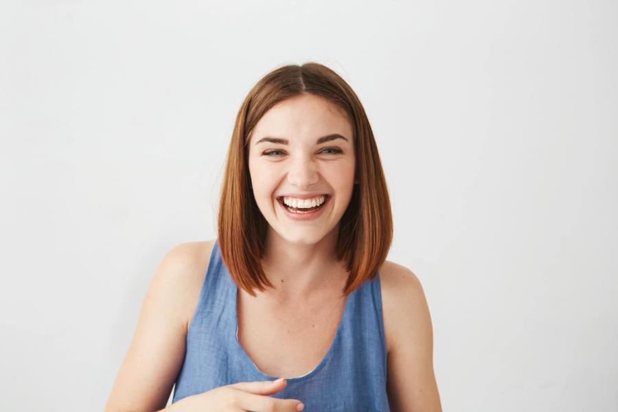 a woman in a blue tank top is laughing and pointing at the camera .