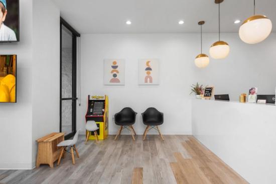 a waiting room at a dental office with two chairs and a video game machine .