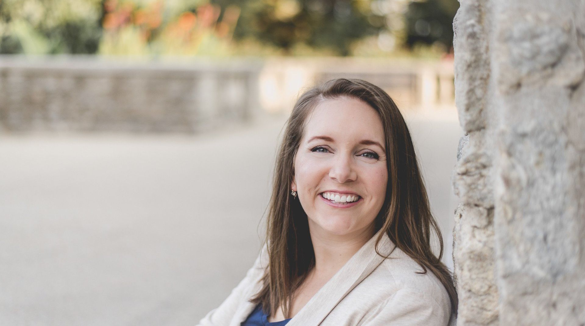 a woman is leaning against a stone wall and smiling .