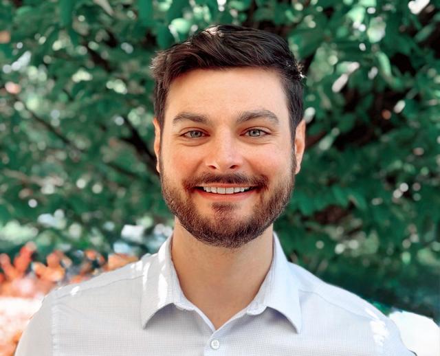 a man with a beard wearing a white shirt smiles for the camera