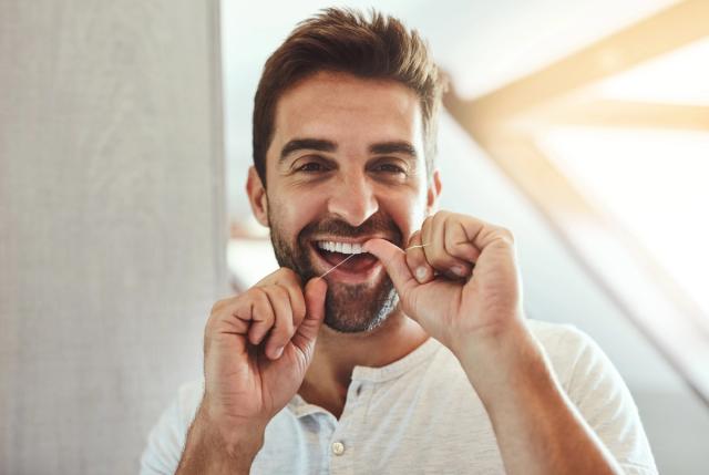 a man is flossing his teeth in front of a mirror .