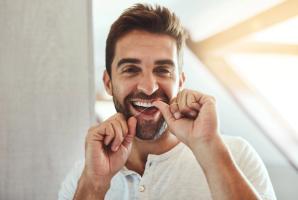 A smiling man flossing his teeth.