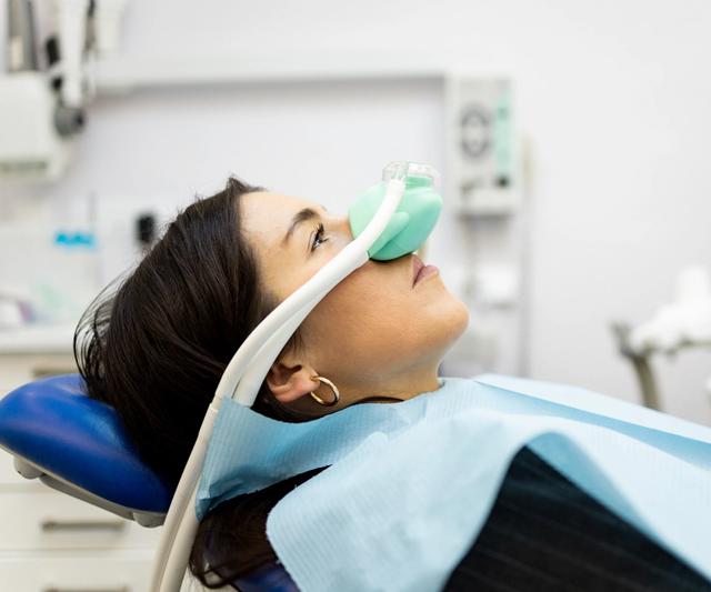 a woman is laying in a dental chair with an oxygen mask on her face .