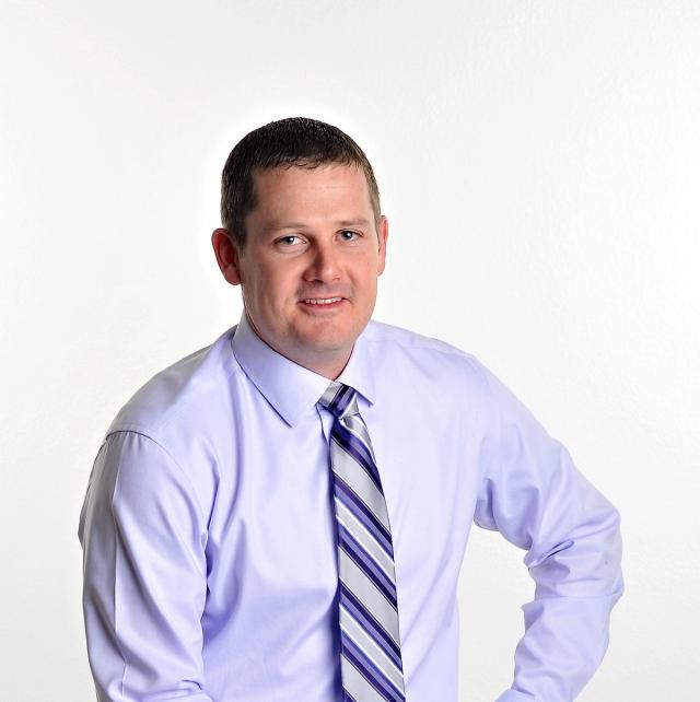 a man in a purple shirt and tie is smiling for the camera .