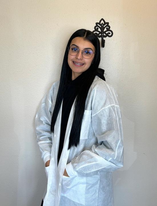 a woman wearing glasses and a white lab coat is standing in front of a wall .